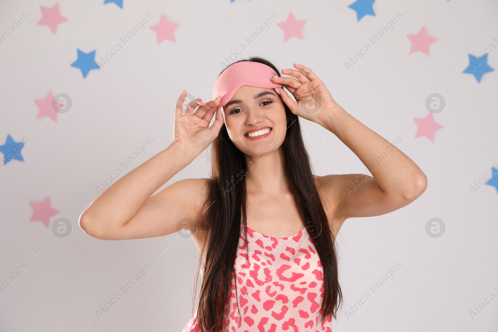 Photo of Beautiful woman wearing sleeping mask on light grey background. Bedtime