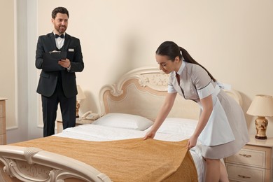 Photo of Man wearing suit with clipboard checking maid's work in hotel room. Professional butler courses