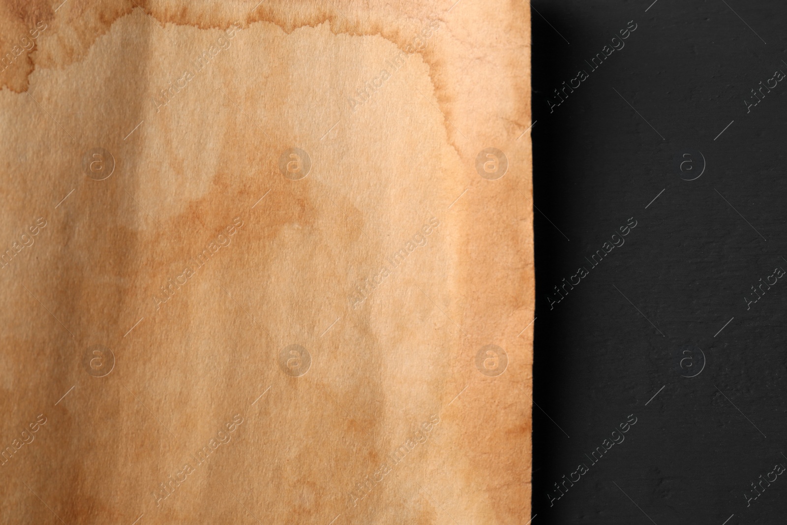 Photo of Sheet of old parchment paper on black wooden table, top view. Space for text