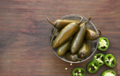 Photo of Fresh and pickled green jalapeno peppers on wooden table, flat lay. Space for text