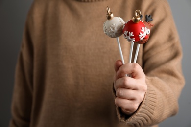 Photo of Woman holding delicious Christmas themed cake pops on grey background, closeup