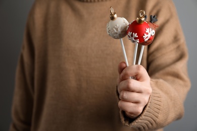 Woman holding delicious Christmas themed cake pops on grey background, closeup