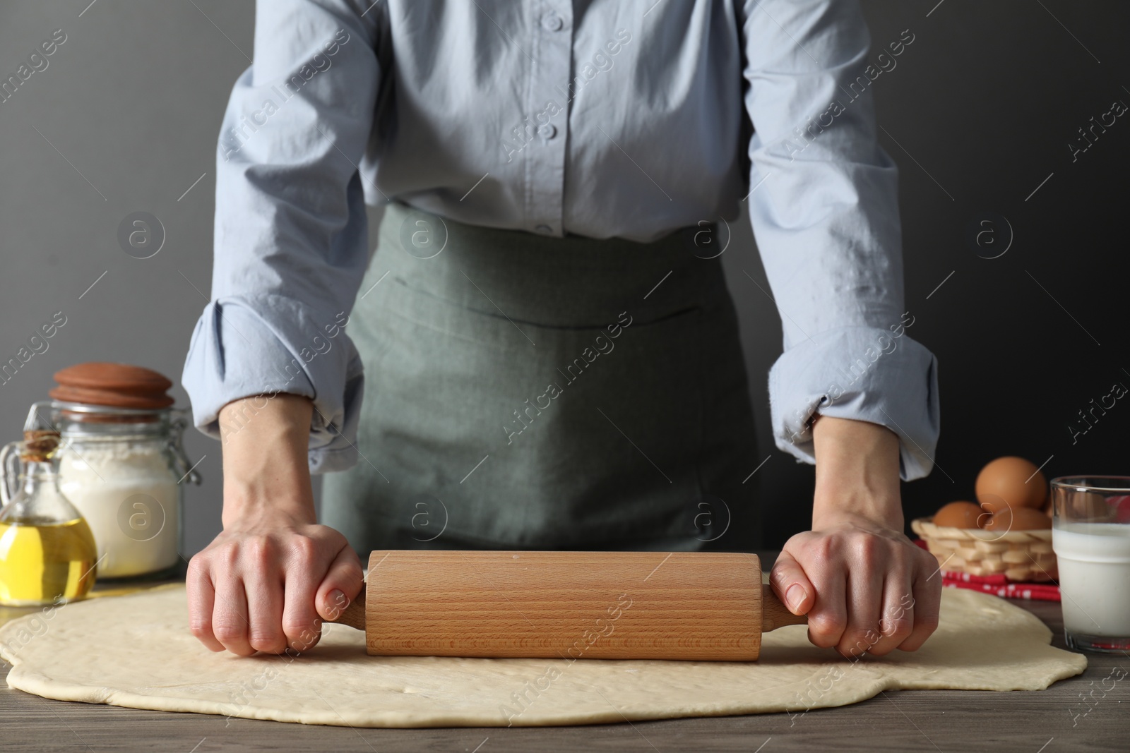 Photo of Woman rolling raw dough at wooden table, closeup