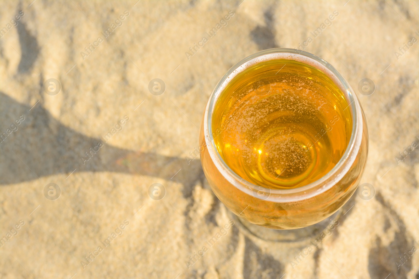 Photo of Above view of glass with cold beer on sandy beach. Space for text