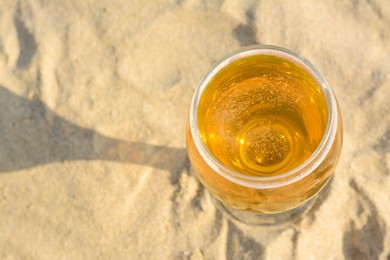 Photo of Above view of glass with cold beer on sandy beach. Space for text
