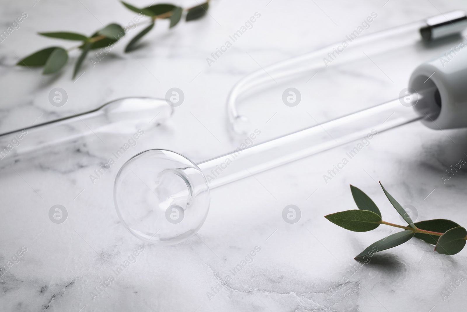 Photo of Modern darsonval with nozzles and tree branches on white marble table, closeup