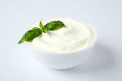 Photo of Bowl of fresh sour cream with basil on white background