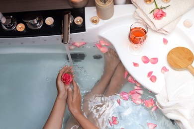 Photo of Woman holding rose flower while taking bath, above view. Romantic atmosphere