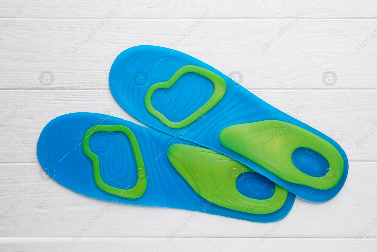 Photo of LIght blue orthopedic insoles on white wooden background, flat lay