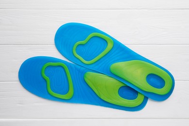 LIght blue orthopedic insoles on white wooden background, flat lay