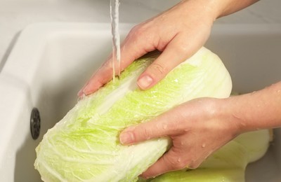 Photo of Woman washing fresh chinese cabbage under tap water in kitchen sink, closeup