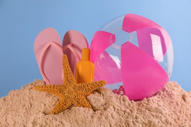 Photo of Beach ball, sunscreen, flip flops and starfish on sand against light blue background