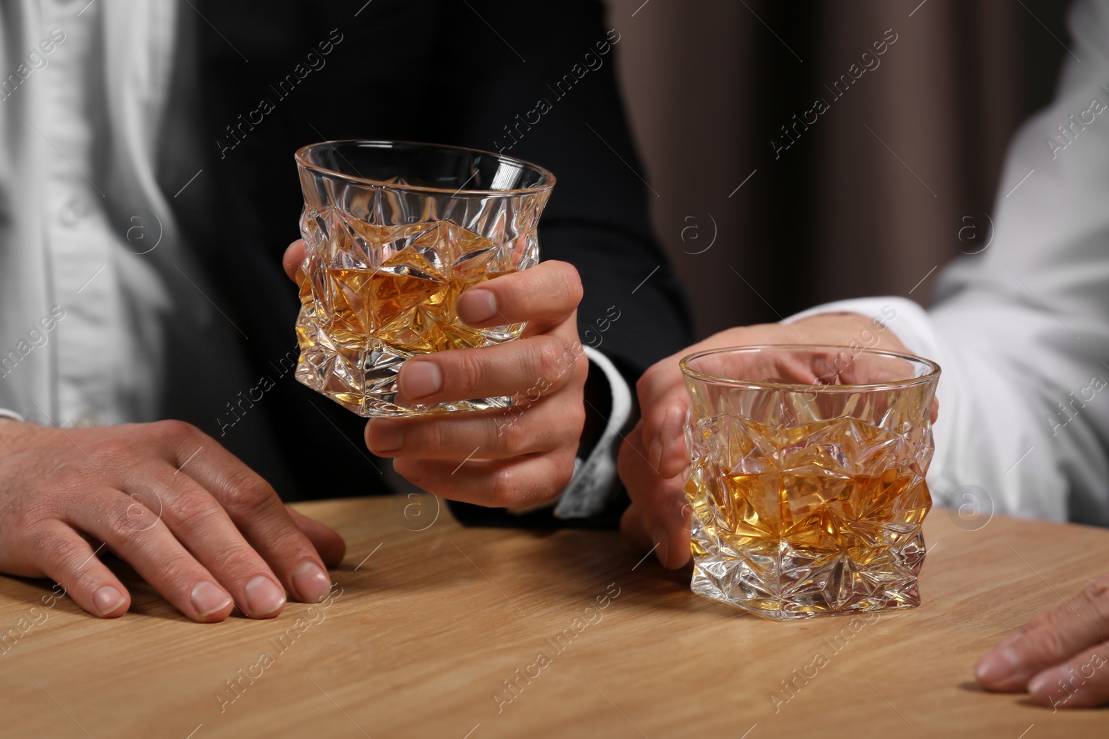 Photo of Men with glasses of whiskey at wooden table indoors, closeup