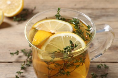 Photo of Glass cup of aromatic herbal tea with thyme and lemon on wooden table, closeup
