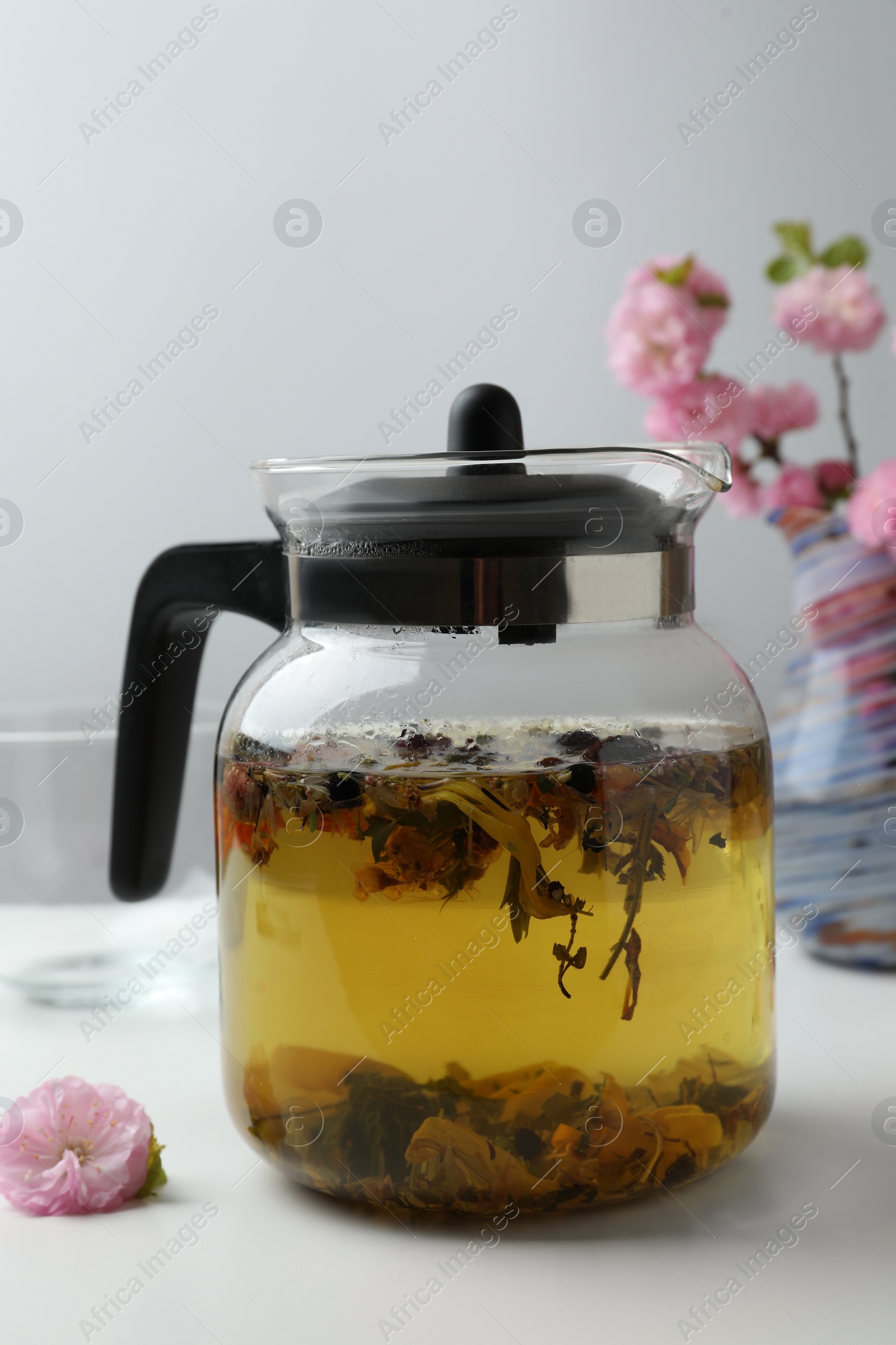 Photo of Glass teapot with freshly brewed tea and beautiful flowers on white table