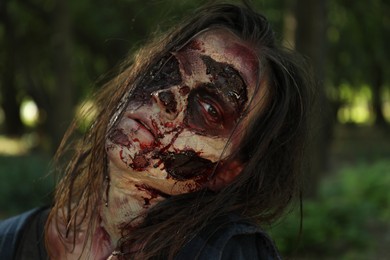 Photo of Scary zombie with bloody face outdoors, closeup. Halloween monster