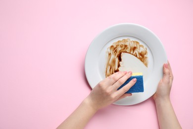 Woman washing dirty plate with sponge on pink background, top view. Space for text