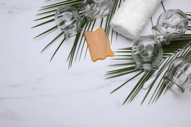 Cupping set, gua sha and green leaves on white table, flat lay. Space for text