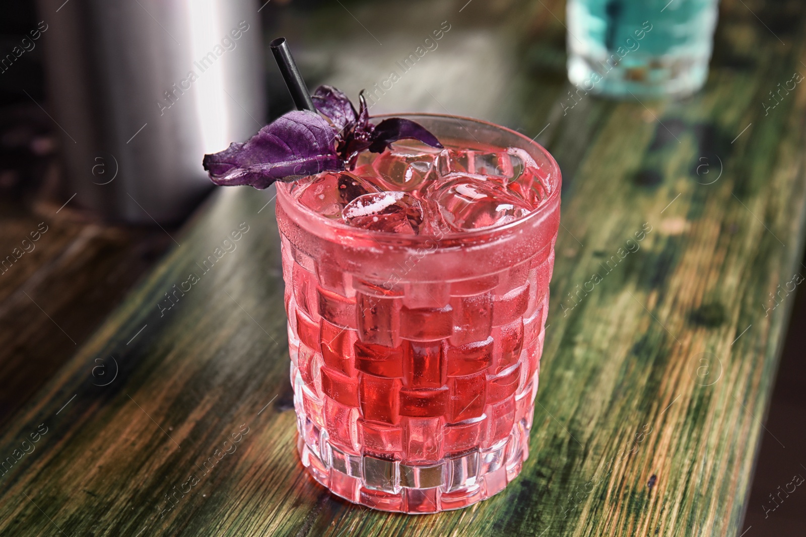 Photo of Glass with delicious cocktail and ice cubes on counter in bar