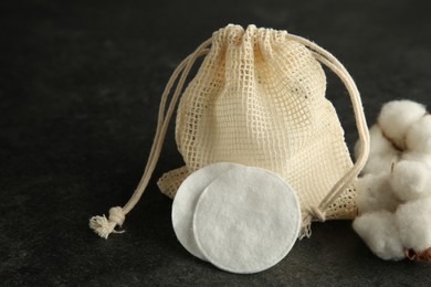 Photo of Cotton pads, bag and flowers on black table, closeup