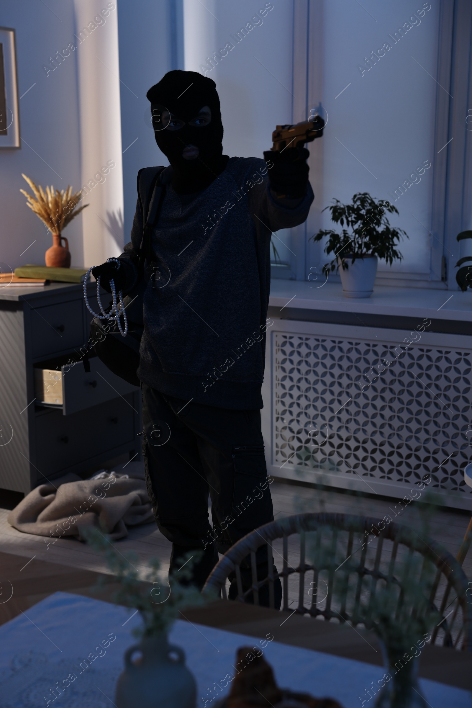 Photo of Thief wearing balaclava with gun and jewels in foreign house. Burglary