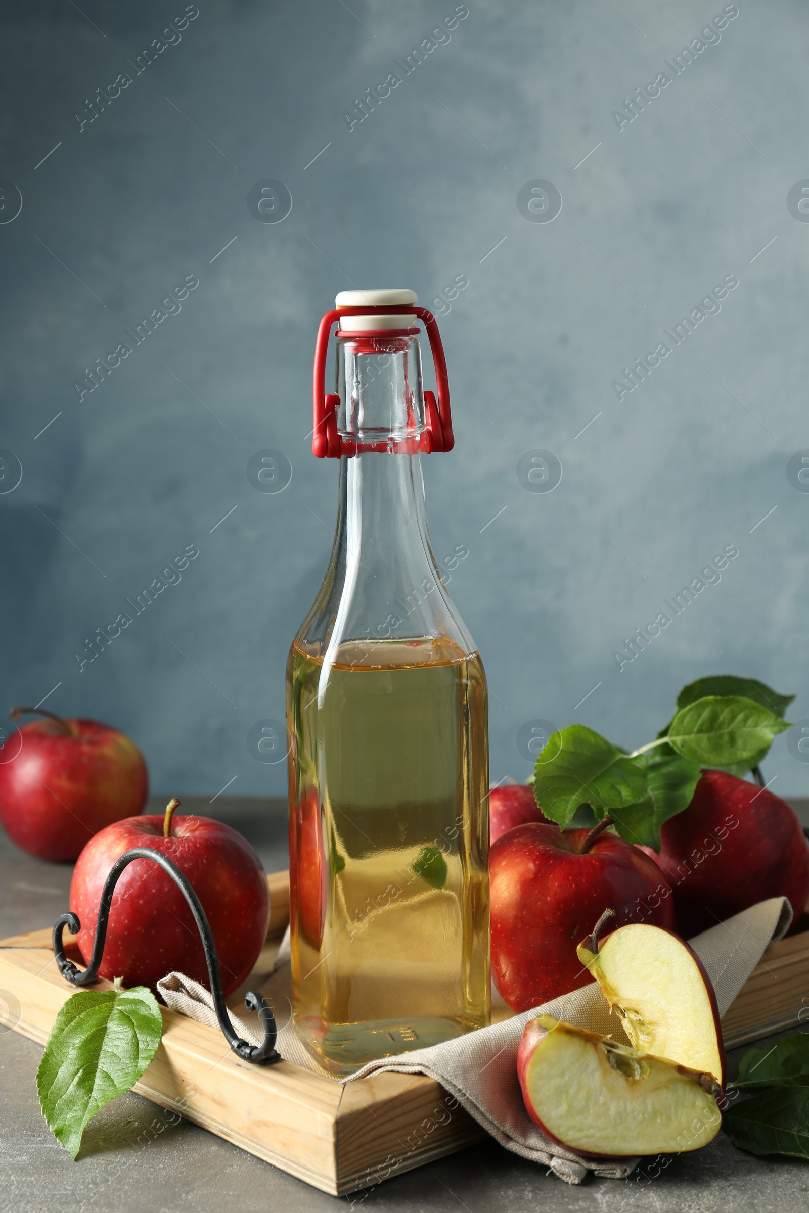 Photo of Bottle of delicious cider and apples with green leaves on gray table