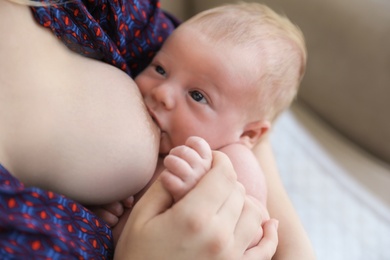 Photo of Woman breast feeding her little baby at home, closeup