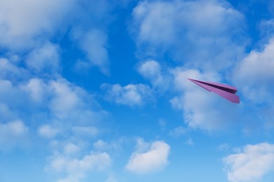 Image of Purple paper plane flying in blue sky with clouds