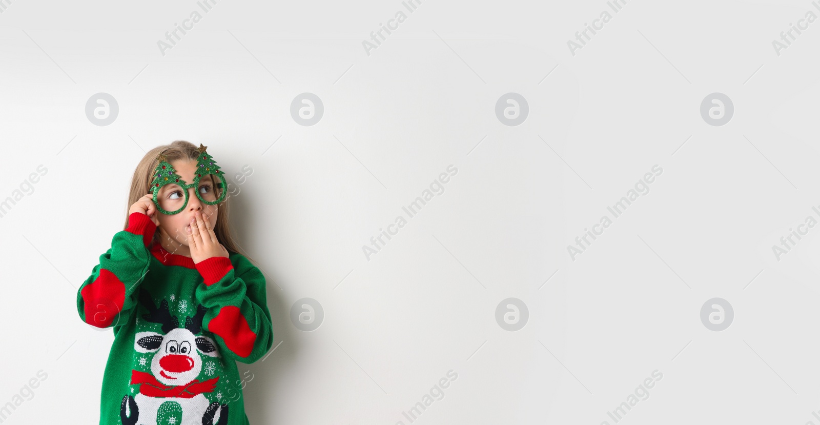 Photo of Cute little girl in Christmas sweater and party glasses on white background, space for text