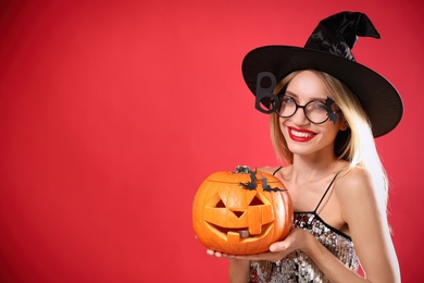 Photo of Beautiful woman in witch costume with jack o'lantern on red background, space for text. Halloween party