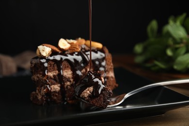 Photo of Pouring sweet syrup onto piece of tasty homemade chocolate cake on plate, closeup