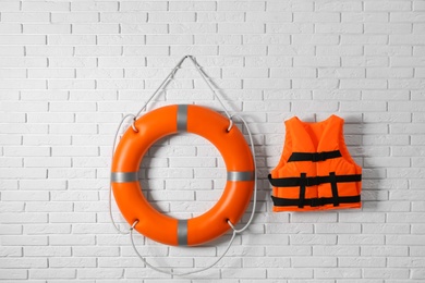 Orange life jacket and lifebuoy on white brick wall. Rescue equipment