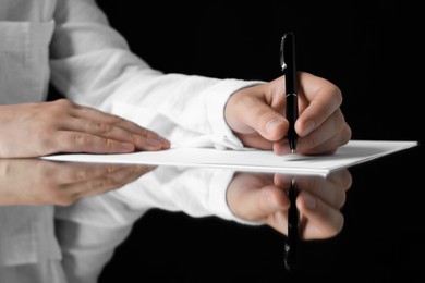 Left handed woman writing on sheet with pen at glass table, closeup