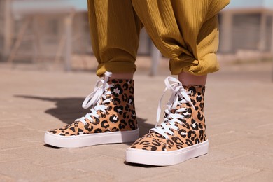 Photo of Woman wearing sneakers with leopard print outdoors, closeup