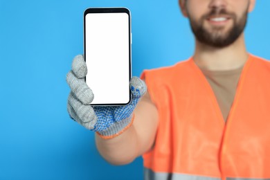 Man in reflective uniform showing smartphone on light blue background, closeup