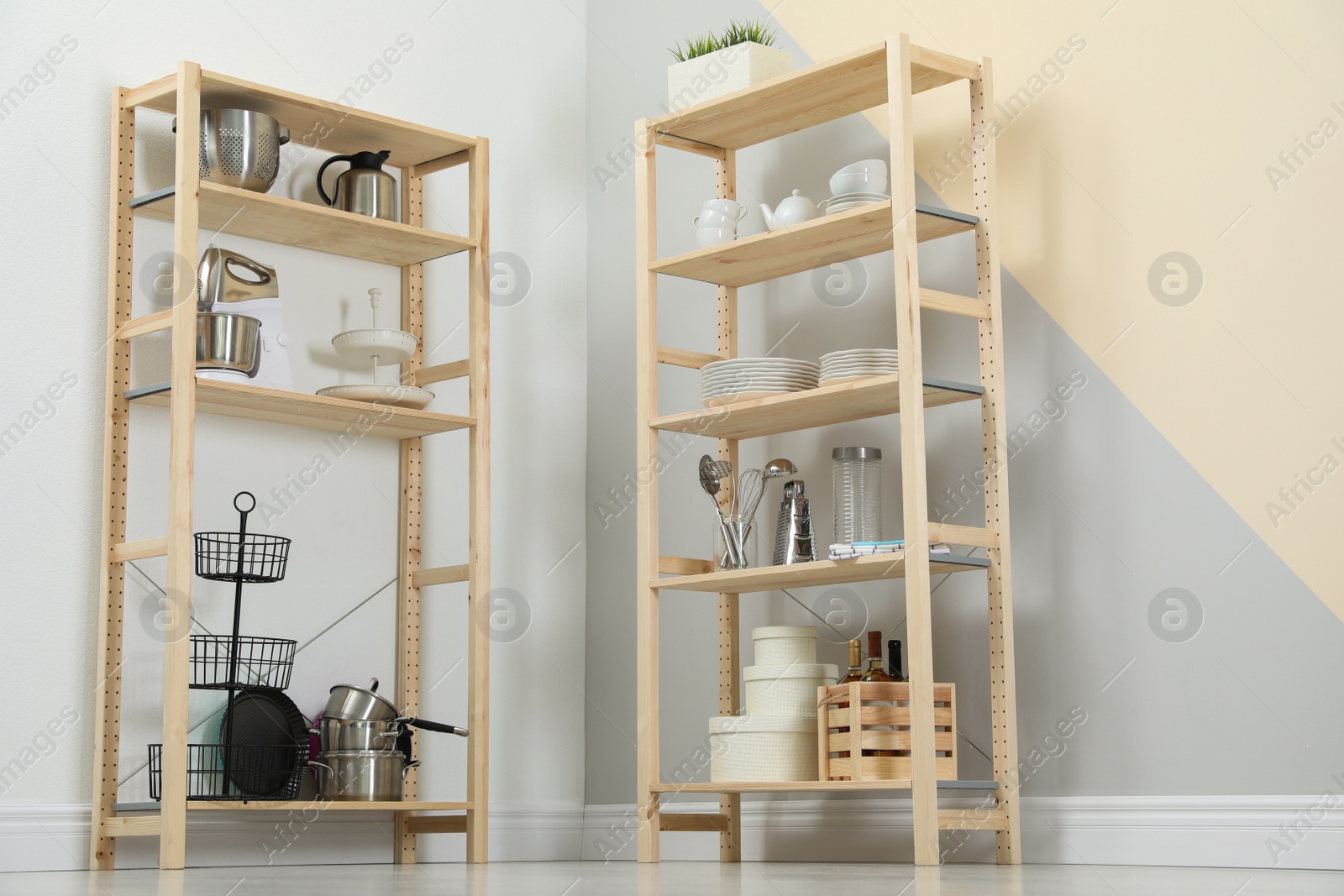 Photo of Wooden shelving units with kitchenware near color wall. Stylish room interior