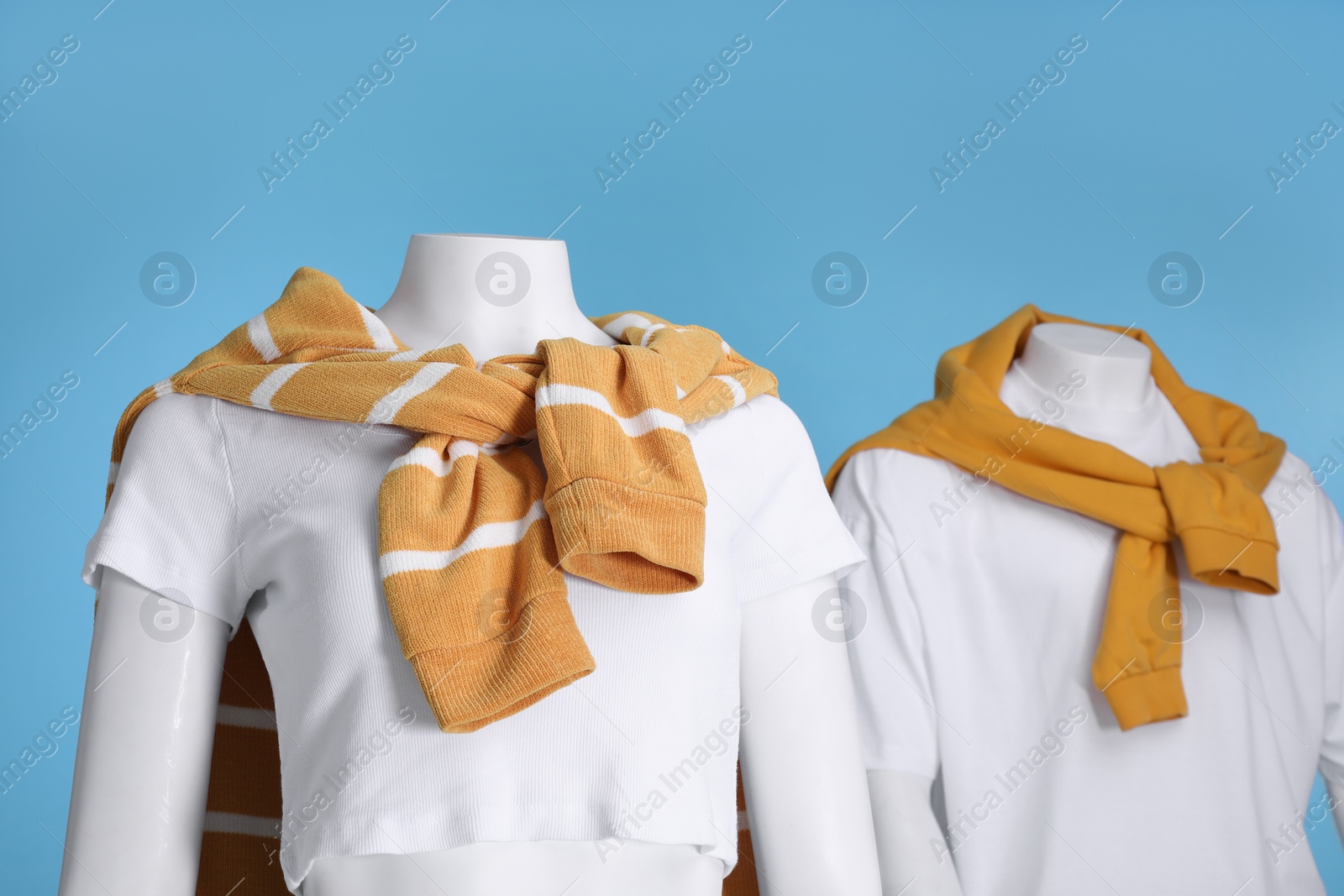 Photo of Female and male mannequins dressed in white t-shirts and orange sweaters on light blue background