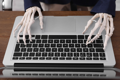Human skeleton in suit using laptop at table, closeup