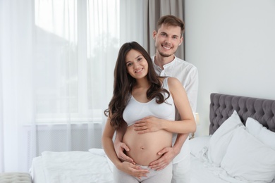 Young husband and his pregnant wife in bedroom. Space for text