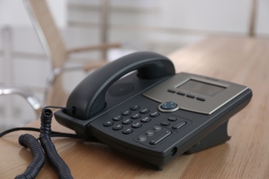 Photo of Desktop telephone on wooden table in office. Hotline service
