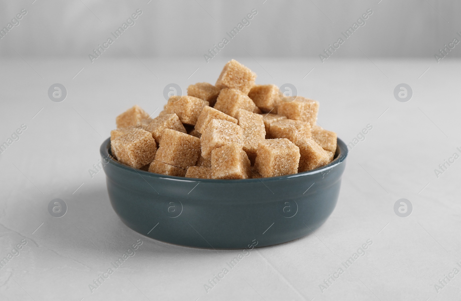 Photo of Brown sugar cubes in bowl on light textured table, closeup