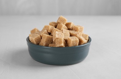 Photo of Brown sugar cubes in bowl on light textured table, closeup