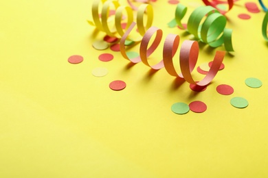 Photo of Colorful serpentine streamers and confetti on yellow background. Space for text