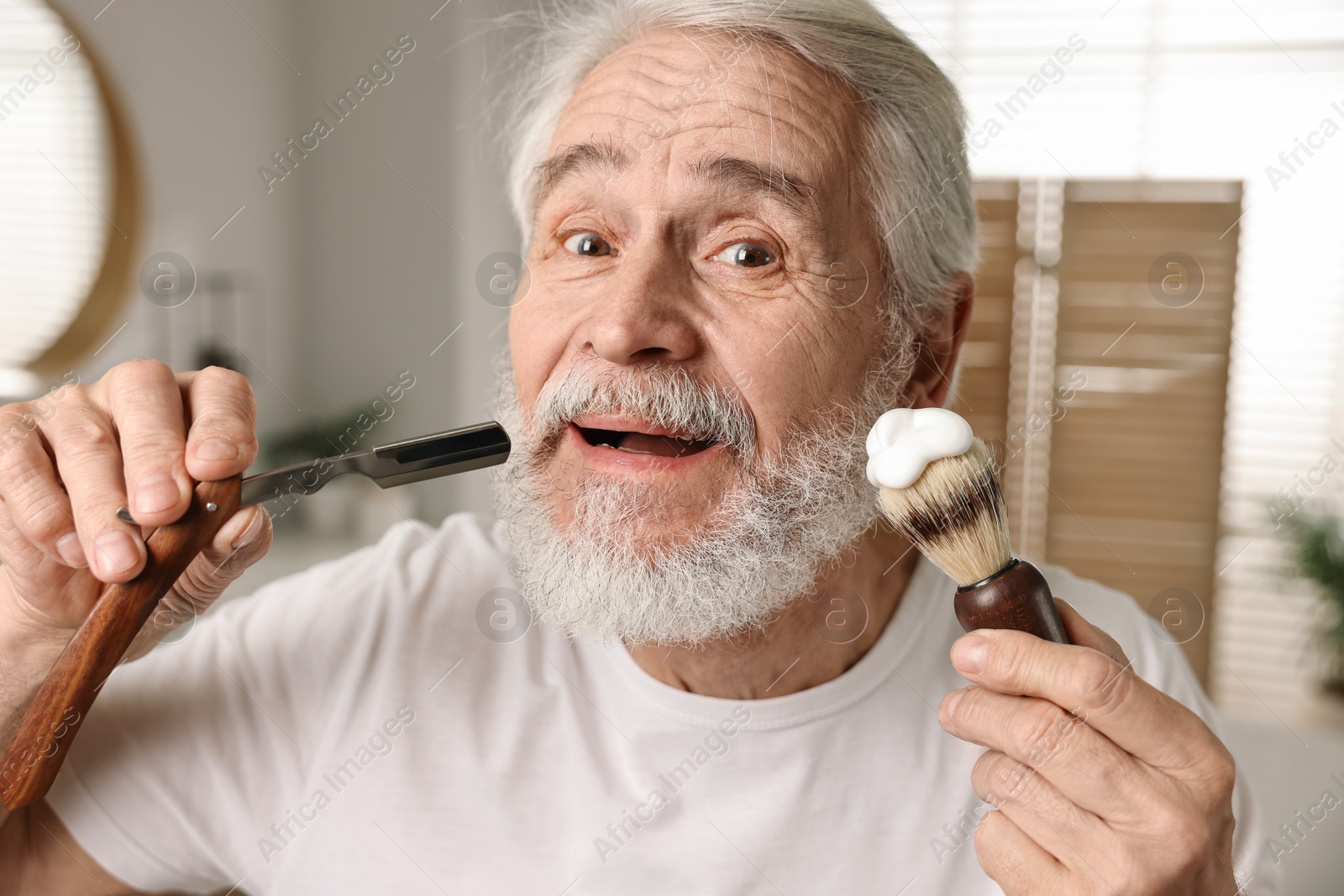 Photo of Man shaving mustache and beard with blade in bathroom