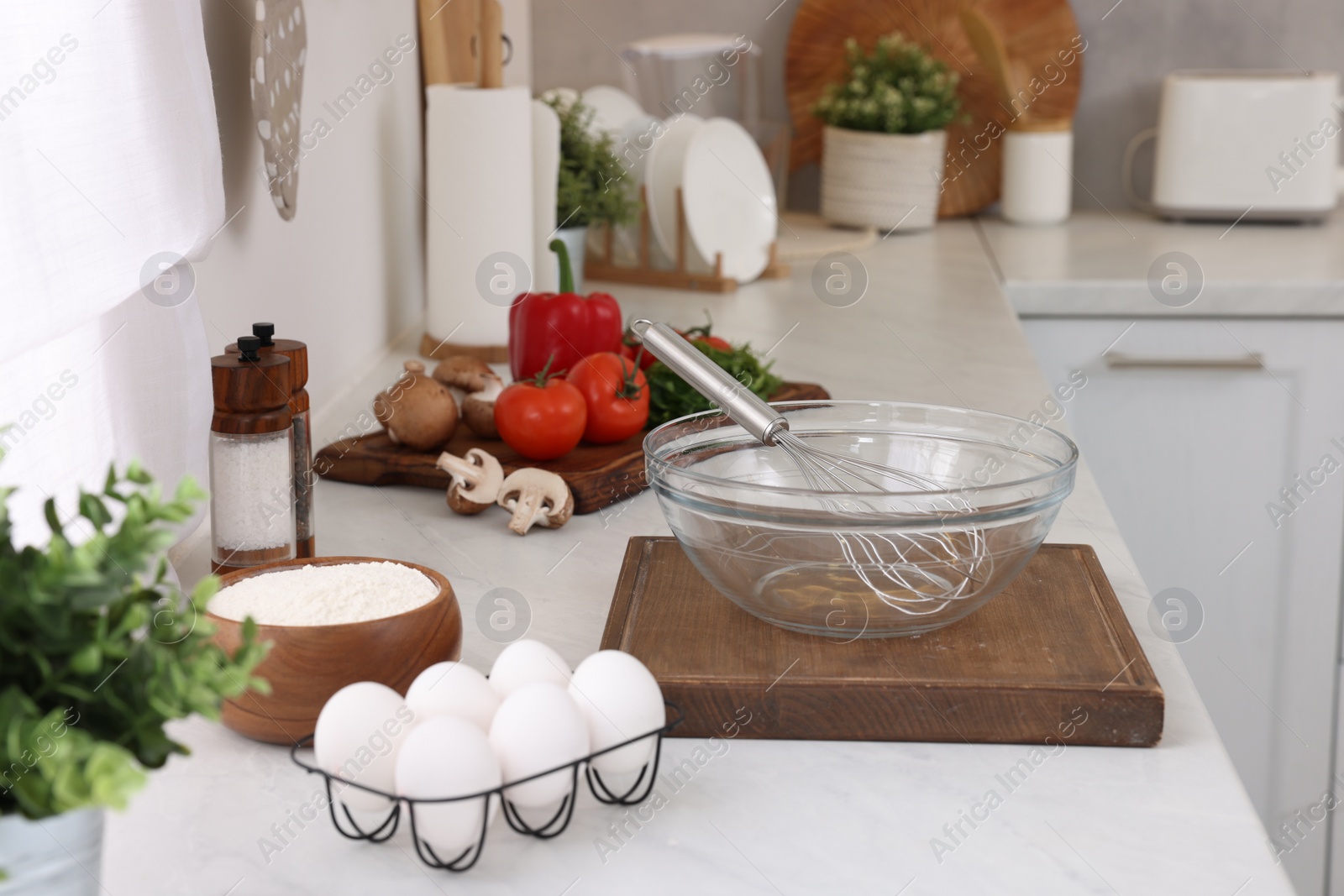 Photo of Metal whisk, bowl and different products on white table in kitchen