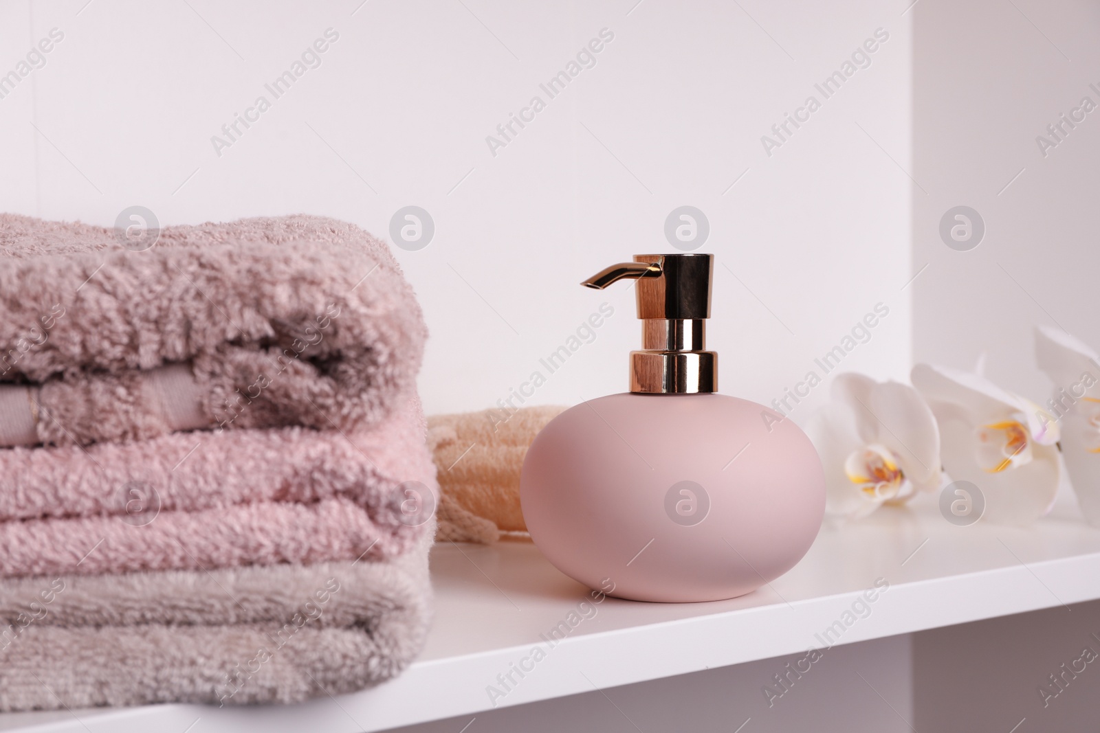 Photo of Stylish soap dispenser with towels and flowers on shelf