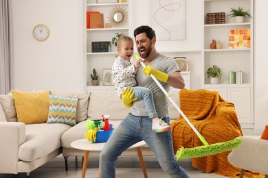 Photo of Spring cleaning. Father and daughter singing while tidying up together at home