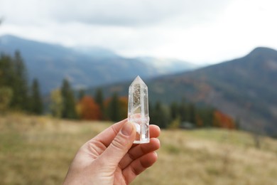 Photo of Woman holding beautiful crystal in mountains, closeup