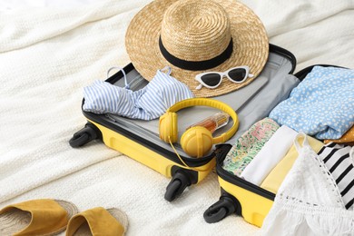 Photo of Open suitcase full of clothes, shoes and summer accessories on bed