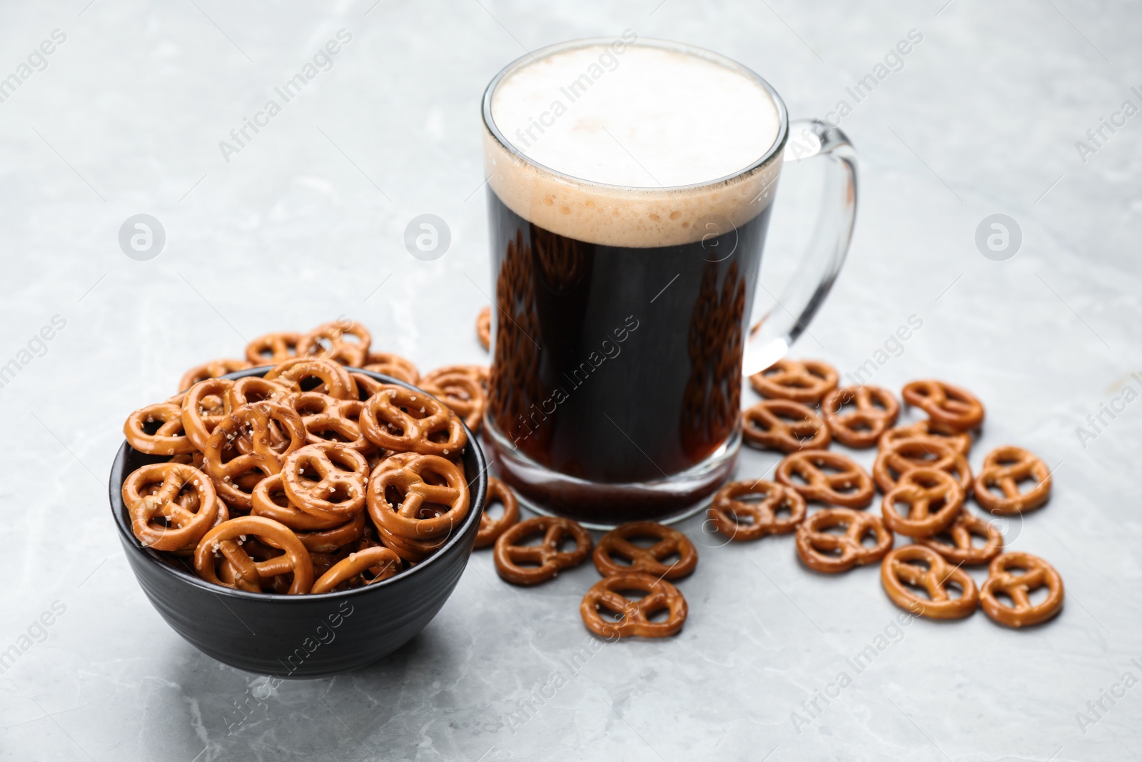 Photo of Delicious pretzel crackers and glass of beer on light grey table